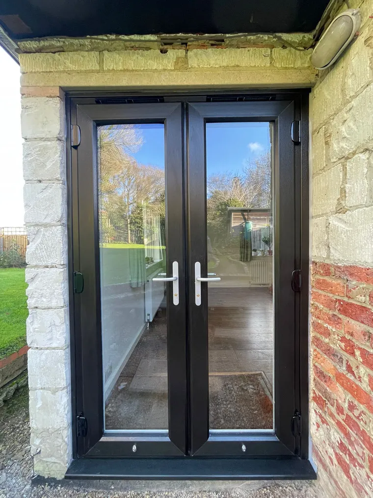 A black double door with a brick wall.